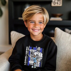 May include: A child wearing a black sweatshirt with a graphic of Lionel Messi. The graphic includes images of Messi in different poses, with text that reads "LEONEL MESSI" and "ANKARA MESSI".