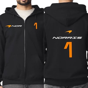 May include: Black zip-up hoodie with the text "NOR" and the number "1" in orange. The front of the hoodie has a logo and the number "1". The back of the hoodie has the name "NORRIS" and the number "1".