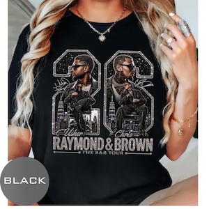 May include: A black t-shirt featuring a graphic print of two men in sunglasses, set within large glittery number frames. The text reads Usher, Chris, Raymond & Brown, and The R&B Tour. The design includes city skylines and star-like sparkles.