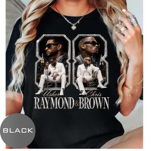 May include: A black t-shirt featuring a graphic print of Usher and Chris Brown. The design includes two large diamond-encrusted number eight frames, each containing images of the artists in white suits. The text reads Usher Raymond & Brown.
