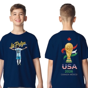 May include: Navy blue t-shirt featuring a soccer player graphic with the text "La Pulga" on the front. The back of the shirt displays the FIFA World Cup trophy, the text "USA 2026", and the flags of Canada and Mexico.
