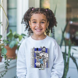 May include: White sweatshirt with a collage of Lionel Messi images and the text "GO!" and "LEONEL MESSI". The design includes images of Messi in different soccer uniforms. The sweatshirt is worn by a young person.