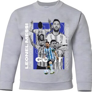 May include: A light grey sweatshirt with a design featuring multiple images of Lionel Messi, wearing the number 10. The design includes the text "LEONEL MESSI" and "ANKARA MESSI" in white, and the words "GO IT".