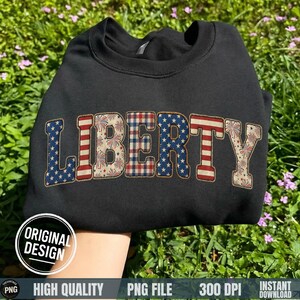 May include: Black sweatshirt with the word "LIBERTY" in a patriotic design. The letters feature patterns of stars, stripes, and fireworks. The sweatshirt is displayed on a bed of green grass.