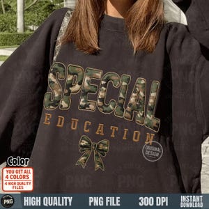 Puede incluir: Sudadera gris oscuro con la palabra "SPECIAL" en estampado de camuflaje y "EDUCATION" en bordado dorado. Un lazo de camuflaje está debajo del texto. La sudadera tiene un diseño vintage.