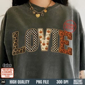 May include: Dark gray t-shirt with the word "LOVIE" in a patchwork design. The letters feature leopard print, checkerboard, and pumpkin patterns. The shirt has a vintage look and includes additional text and graphics.