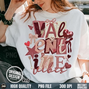 May include: White t-shirt with a Valentine's Day design. The design features the words "VALENTINE VIBES" in shades of red and pink, with hearts, bows, and a star. The shirt has a crew neck and short sleeves.