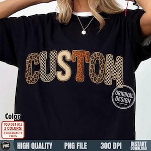 May include: Black t-shirt with the word "CUSTOM" in a bold, decorative font. The letters have a mix of leopard print, checkered, and tan designs. The shirt also has the text "ORIGINAL DESIGN" in a circle.