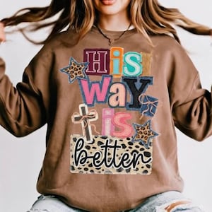 Könnte beinhalten: Ein braunes Sweatshirt mit dem Text "His Way Is Better" in einem Patchwork-Design. Der Text enthält ein Kreuz, Sterne und Leopardenmuster. Das Sweatshirt ist ein lässiger, bequemer Stil.