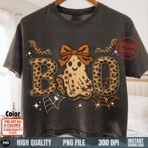 May include: Dark gray t-shirt with a Halloween-themed design. The word "BOO" is spelled out with leopard print letters. A ghost with a bow and bats are featured. Includes spiderwebs and stars. The shirt has the text "ORIGINAL DESIGN".