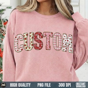 May include: A light pink sweatshirt with the word "CUSTOM" in a variety of patterns. The letters are decorated with hearts, roses, leopard print, and gingham. The sweatshirt is a solid light pink color.