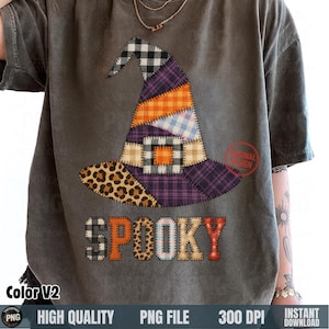 May include: Dark gray t-shirt featuring a patchwork witch hat design with leopard print, plaid, and orange accents. The word "SPOOKY" is printed below the hat in a patchwork style. The shirt is a relaxed fit.