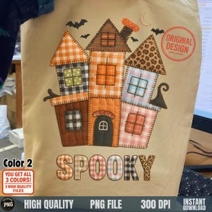 May include: A beige tote bag featuring a patchwork house design with orange, brown, pink, and blue squares. The word "SPOOKY" is below the house. The design includes bats, a crescent moon, and the text "ORIGINAL DESIGN".