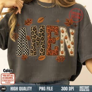 Könnte beinhalten: Dunkelgraues T-Shirt mit dem Wort "AMEN" in dekorativer Schrift. Der Buchstabe "A" ist kariert, "M" ist Leopardenmuster, "E" ist orange und "N" hat Kürbisgrafiken. Herbstblätter und Sterne umgeben das Wort.