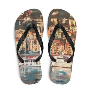 May include: A pair of flip-flops with a painting of a coastal town, featuring colorful buildings and boats. The flip-flops have black straps and the word "MILADY" is printed on the right flip-flop.
