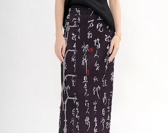 May include: A black pleated top and a black skirt with white calligraphy print. The skirt has a high waist and falls to the mid-calf. The outfit is paired with white flats.