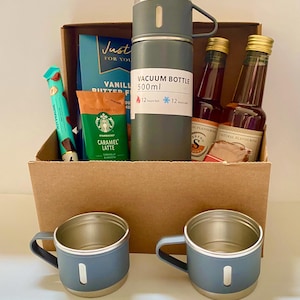 May include: A gift basket with a gray vacuum bottle, two blue mugs, and various food items. The vacuum bottle has a 500ml capacity and keeps contents hot or cold for 12 hours. The basket includes Starbucks Caramel Latte and vanilla butter fudge.