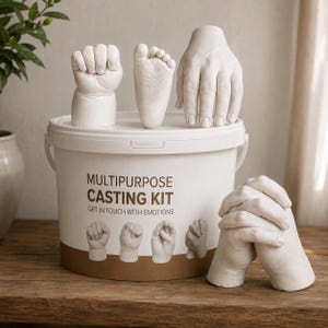 May include: A white plastic bucket labeled MULTIPURPOSE CASTING KIT GET IN TOUCH WITH EMOTIONS with white plaster sculptures of a baby fist, a baby foot, an adult hand, and two clasped hands displayed on and beside the container lid.