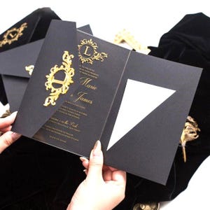 Pode incluir: Um convite de casamento preto com letras em folha de ouro e um emblema decorativo de filigrana dourada na aba frontal. O cart&atilde;o exibe os nomes Marie e James com detalhes do evento impressos em tinta dourada sobre um fundo preto fosco.