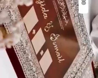 May include: A maroon wedding invitation with silver embellishments and the names "Majida & Ismail" in gold lettering. The invitation has a decorative border and includes the text "NIKAH & RESIN STUDIO". A phone number is also visible.