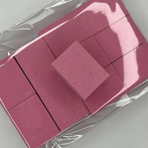 May include: A pack of pink makeup sponges in a clear plastic bag. The sponges are rectangular and square, with a slightly textured surface. The background is a light grey.
