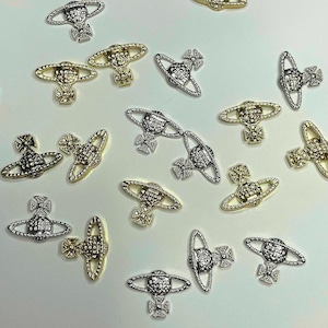 May include: An assortment of silver and gold-toned metal charms, each featuring a distinctive orb and cross design. The charms are scattered across a white surface, showcasing their intricate details and varying finishes. These decorative charms are ideal for jewelry making.