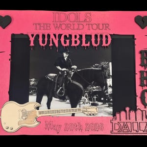 Puede incluir: Un marco de fotos rectangular de color rosa con el texto IDOLS THE WORLD TOUR YUNBLUD, May 28th 2026 y DALLAS. El marco incluye corazones negros, un recorte de guitarra de madera y las letras BHC, rodeando una foto en blanco y negro de una persona a caballo.