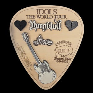 May include: A guitar pick-shaped wooden plaque featuring the text IDOLS THE WORLD TOUR, Yungblud, ZOMBIE, and STURGIS CHIP Buffalo Chip 8-9-2026. It includes a silver-toned electric guitar, a motorcycle, and two black broken heart icons.
