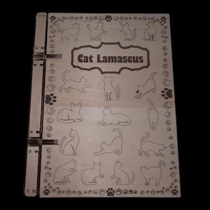 Puede incluir: Una caja de madera con un lado con bisagras y un tema decorativo de gatos. La caja presenta el texto "Cat Lamascus" y múltiples siluetas de gatos. Huellas de patas bordean los bordes de la caja.