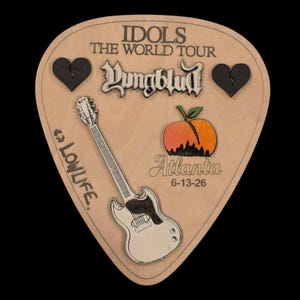 May include: A guitar pick-shaped wooden plaque featuring the text IDOLS THE WORLD TOUR, Yungblud, LOWLIFE, and Atlanta 6-13-26. It includes two black broken heart icons, a white electric guitar illustration, and a peach graphic with a city skyline.