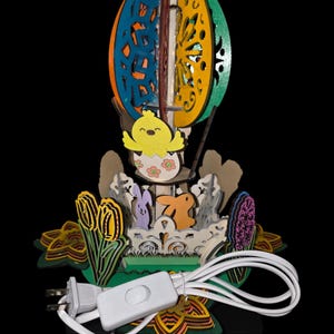 May include: A colorful Easter-themed wooden lamp featuring a hot air balloon design. The lamp includes a yellow chick, rabbits, and floral accents. The lamp has a white cord with a switch and a standard US plug.