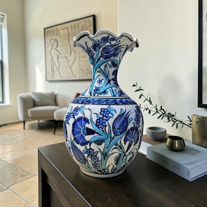 Puede incluir: Un jarrón de cerámica con base blanca y un patrón floral pintado a mano en tonos azul oscuro y turquesa. El jarrón presenta un cuerpo bulboso, un cuello estrecho y un borde festoneado, decorado con intrincados motivos de tulipanes y flores.