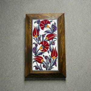 May include: A framed floral tile with a design of red tulips and flowers with yellow centres, set against a white background. The artwork is framed in a dark brown wooden frame, creating a decorative piece.