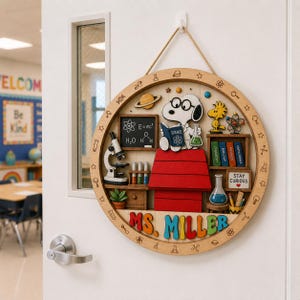 May include: A circular wooden wall sign featuring a cartoon dog wearing glasses and a lab coat, sitting on a red doghouse. The sign includes a chalkboard with science formulas, a microscope, test tubes, books, and the text MS. MILLER in colorful letters.