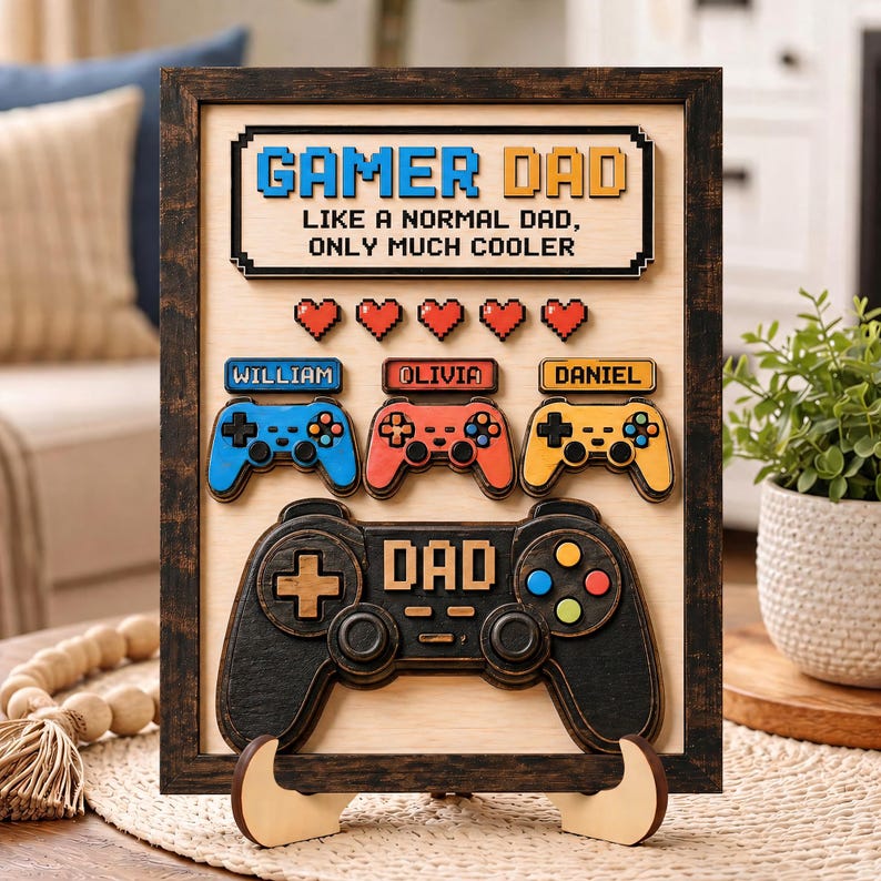 May include: A rectangular wooden sign with a dark frame featuring the text GAMER DAD LIKE A NORMAL DAD, ONLY MUCH COOLER. It includes five red pixelated hearts, three smaller game controllers labeled William, Olivia, and Daniel, and one large black controller labeled DAD.
