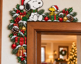 May include: A decorative Christmas door corner sign featuring Snoopy wearing a Santa hat and a green and red striped scarf, sitting next to Woodstock in a Santa hat. The design includes pine branches, holly, red berries, pinecones, and wrapped gifts.