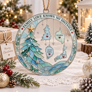 Peut inclure: Une décoration circulaire ornée d'un sapin de Noël style vitrail dans des tons bleu et vert, agrémenté de perles et d'étoiles. Elle porte l'inscription FAMILY LOVE KNOWS NO DISTANCE et quatre cartes suspendues du Royaume-Uni, de la Colombie, de la Corée du Sud et du Japon, chacune marquée d'un petit cœur rouge.