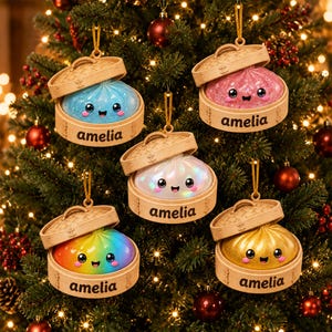 May include: Five round dumpling ornaments in bamboo steamer baskets, each featuring a smiling face and the name amelia printed on the side. The dumplings are blue, pink, iridescent white, rainbow, and gold, all with glittery finishes.