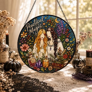 May include: A circular stained glass suncatcher featuring the text Practical Magic, depicting two figures with long hair surrounded by flowers, a bottle labeled Rose Petals, a candle, a mortar and pestle, and books labeled Herbs, Spells, and Remedies.