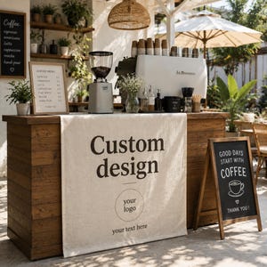 May include: A rustic wooden coffee bar counter draped with a beige linen fabric banner featuring the printed text Custom design, a circular logo placeholder, and your text here. The counter holds a coffee grinder, espresso machine, and menu board.
