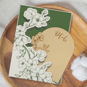May include: A rectangular invitation card with a dark green background and a white die-cut overlay featuring a detailed line drawing of cherry blossoms. A tan arch-shaped insert card with the word Details in script is tucked behind the overlay.
