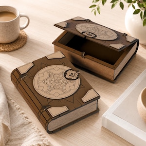 May include: Two rectangular wooden boxes designed to resemble vintage books. Each box features a dark brown finish with a lighter wood circular emblem on the cover, displaying geometric patterns and a central star motif with corner accents.