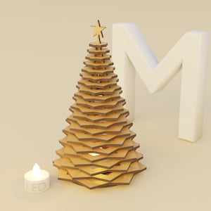 Op de afbeelding: Een houten kerstboom met een ster op de top, gemaakt van gelaagde geometrische vormen. Een kleine LED-kaars staat voor de boom en een witte letter "M" staat op de achtergrond. De boom is ongeveer 20 cm hoog.