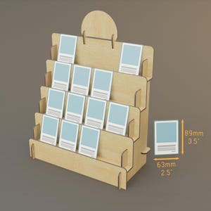 Peut inclure: Un présentoir en bois clair à plusieurs étagères en gradins, conçu pour contenir de petites cartes ou des impressions. Le présentoir a un dessus arrondi. Chaque carte mesure 8,9 cm de haut et 6,3 cm de large.