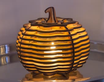 Puede incluir: Una linterna decorativa con forma de calabaza construida con capas de madera apiladas y cortadas con láser, con un interior de color claro natural y bordes oscuros quemados. Una luz cálida emana del centro, iluminando los espacios horizontales.