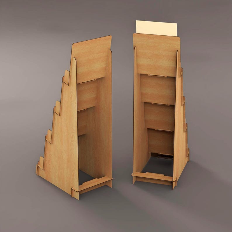 May include: Two wooden display stands with multiple shelves and a stepped design. The stands are made of light-colored wood and are designed to hold products. One stand has a blank sign at the top. The stands are on a gray background.