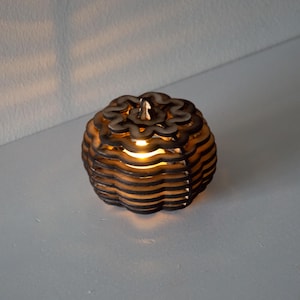 Peut inclure: Un photophore décoratif en bois en forme de citrouille. La citrouille est faite de bois découpé au laser en couches, avec une lumière chaude émanant de l'intérieur. Le design présente un dessus festonné et un corps rond.