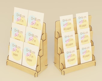 May include: Two wooden display stands holding cards. The cards are labeled with dimensions in inches and centimeters. The cards have a pastel design. The stands are made of light-colored wood.