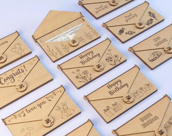 May include: A collection of wooden gift card holders with various engraved designs and text. Some holders say "Happy Birthday," "Congrats!," and "Love You." Others feature images of a cupcake, candy, and a car. Each has a button closure.