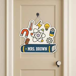 Puede incluir: Un letrero blanco para puerta con ilustraciones de temática científica, incluyendo un termómetro, un átomo y una bombilla. El letrero tiene forma de nube y lleva el texto "MRS. BROWN" en un libro azul. Cuelga de un gancho negro.